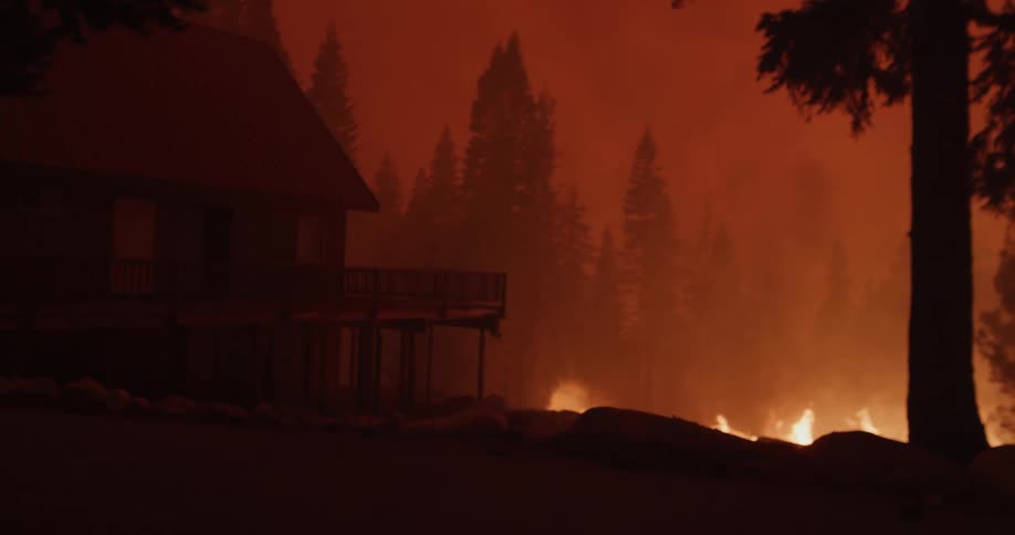 A house sits at the edge of an embankment as a forest fire burns below the red smoke filling sky