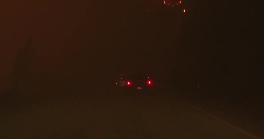 Cars moves slowly through thick smoke on road that passes wildfires