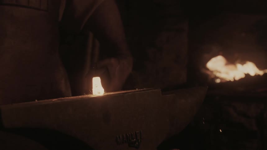 A man is hammering hot metal on an anvil