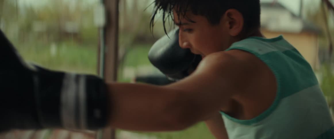 A boy sweats as he punches a heavy bag training wearing boxing gloves