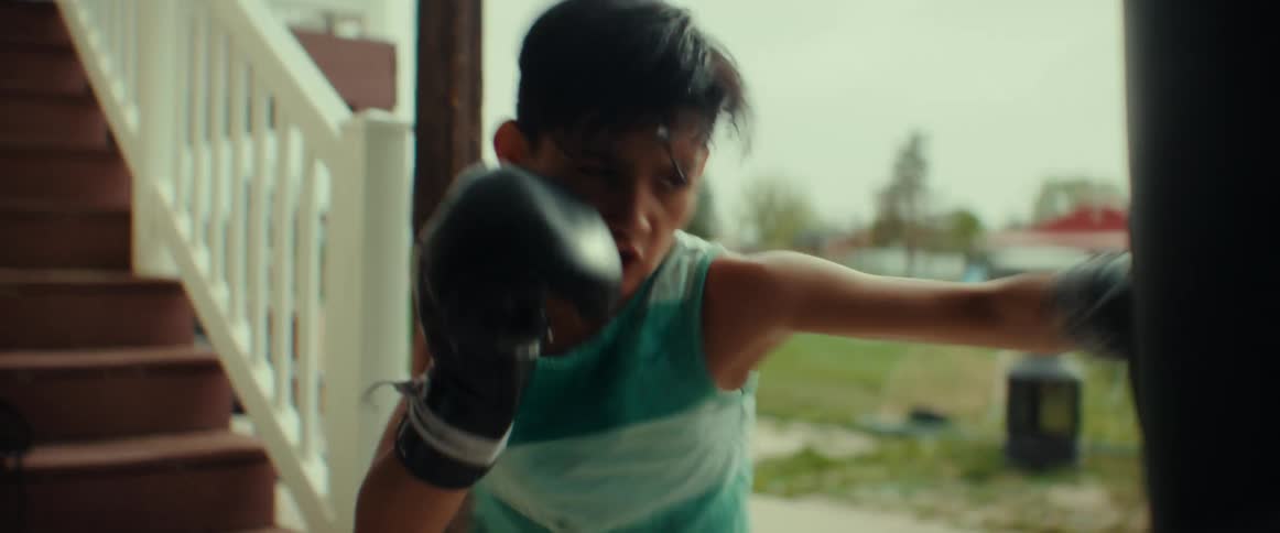 A young boy wearing boxing gloves trains by hitting a hanging heavy bag