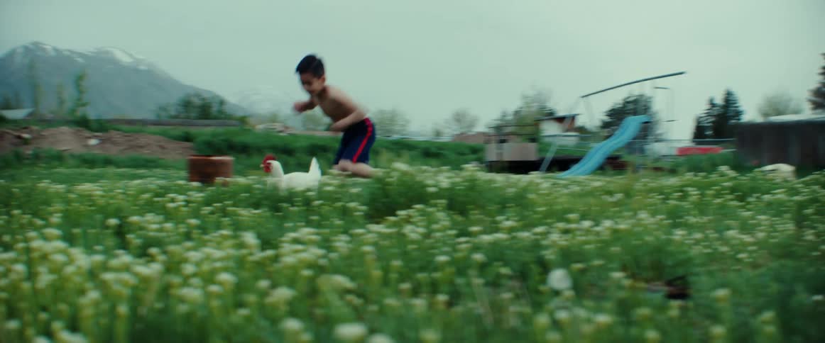 Shirtless boy wearing black shorts chases chicken in the garden