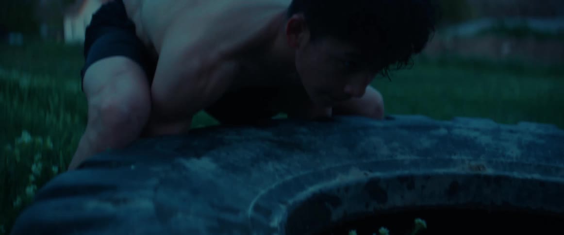 Muscular boy wearing black shorts pushes tire in the garden