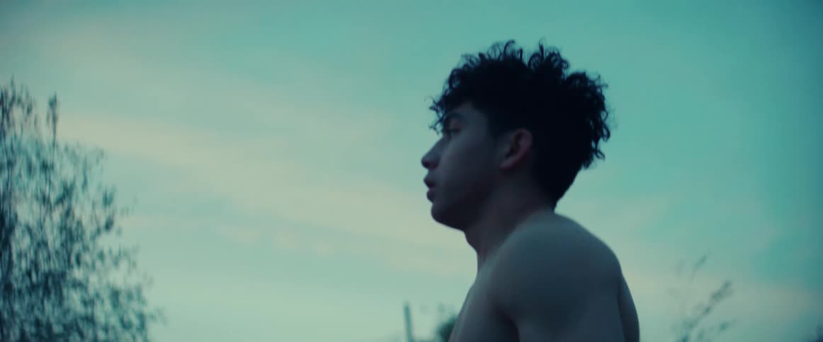 A teenage boy without a shirt on pulls his hands away from his head as he breathes heavily