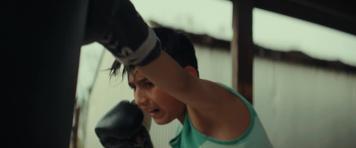 Young sweaty boy practices boxing with a punching bag outdoors