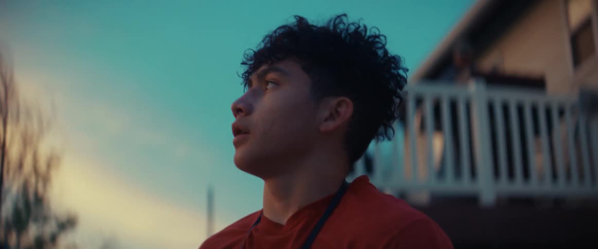 A teenage boy is standing outside of his house looking around in deep thought
