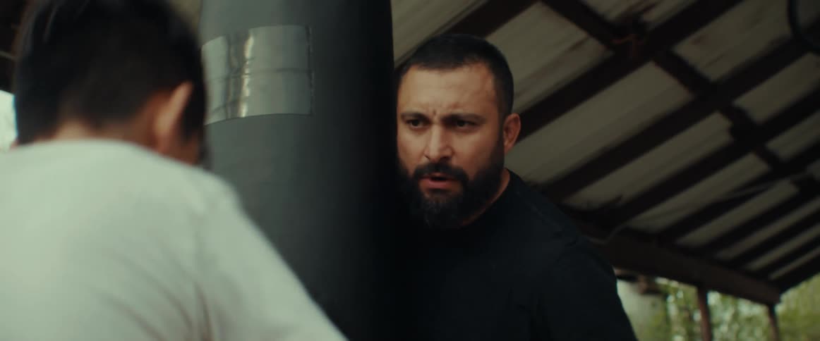Box teacher coaches a young boy practicing on a punching bag hanging on the backyard