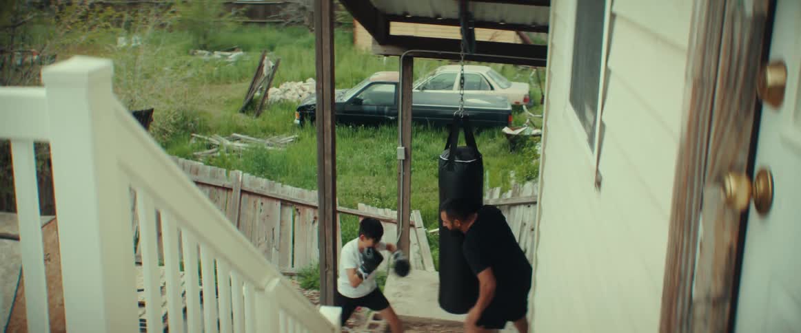A dad holds the hanging heavy bag for his son as he hits and punches it