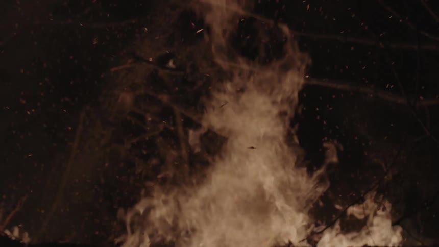 A fire rages burning logs at night