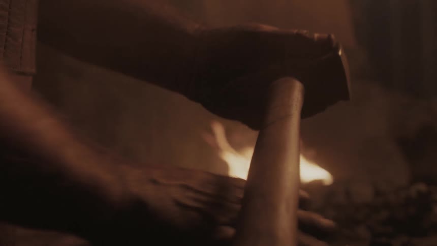 A man polishes his hammer near a fire