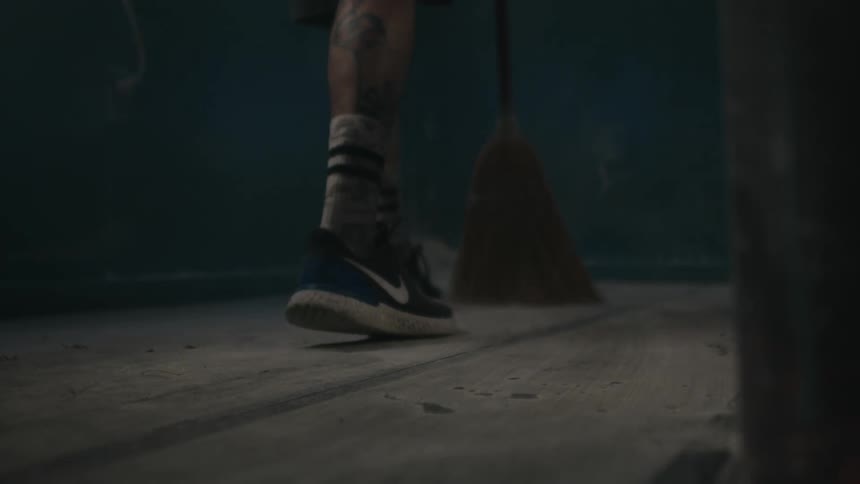 Man with tattoo uses straw broom to sweep dust into corner