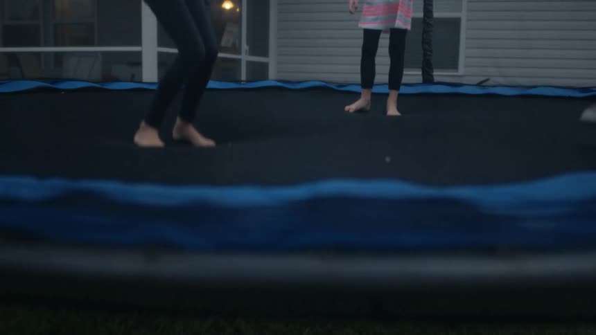 A group of children jump on a trampoline together in the yard of a house during the day