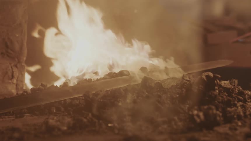 A sword lying on hot coals in front of a fire
