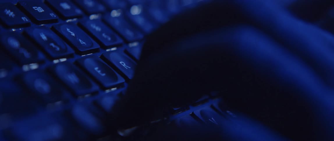 Close up of mans hands typing on computer keyboard in dark room