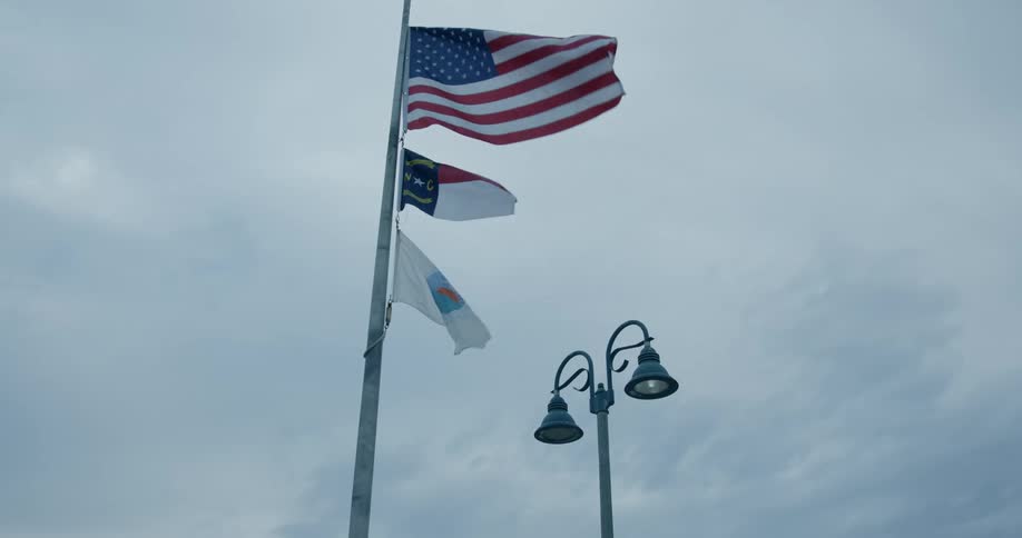 An american flag flies on a pole above two smaller flags as they move in the breeze