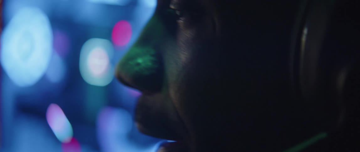 Close up of an operator sitting on a dimly lit room near a bright screen talks on a headset microphone