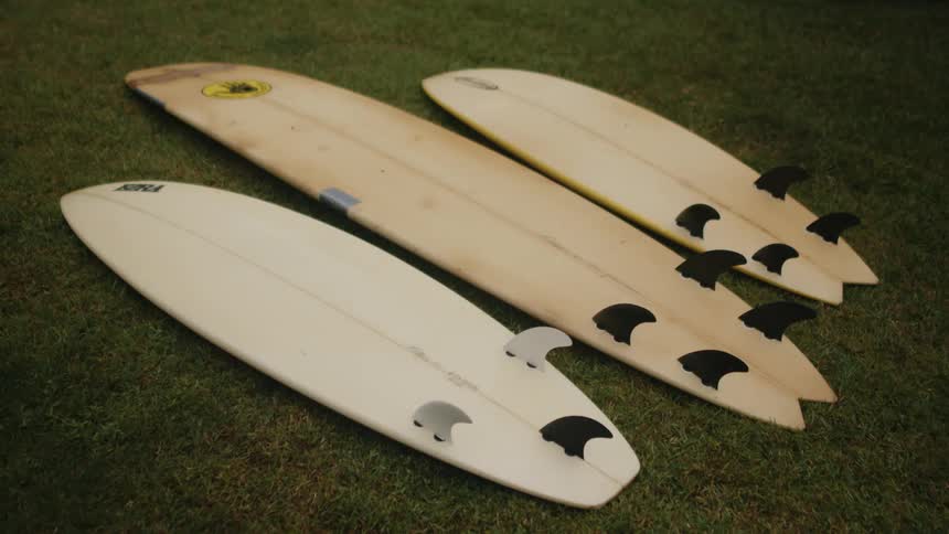 Three surfboards sit face down in a yard side by side