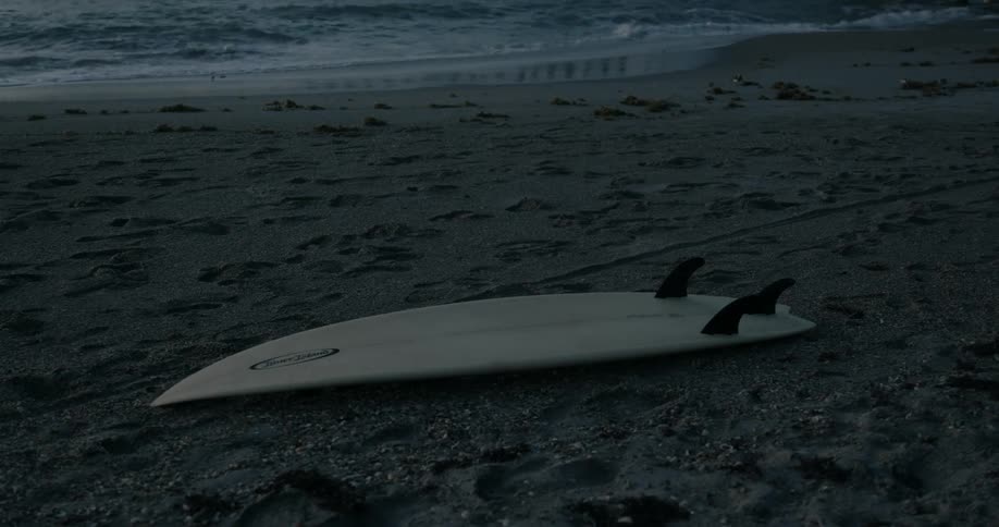 Surfboard lying on the beach near the sea at sunset