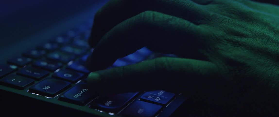 A man types on his computer under a color changing light