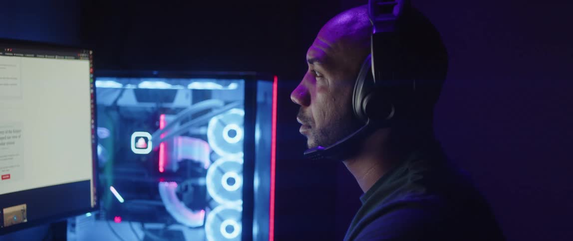 A man in an office with headphones and a microphone looks at his computer