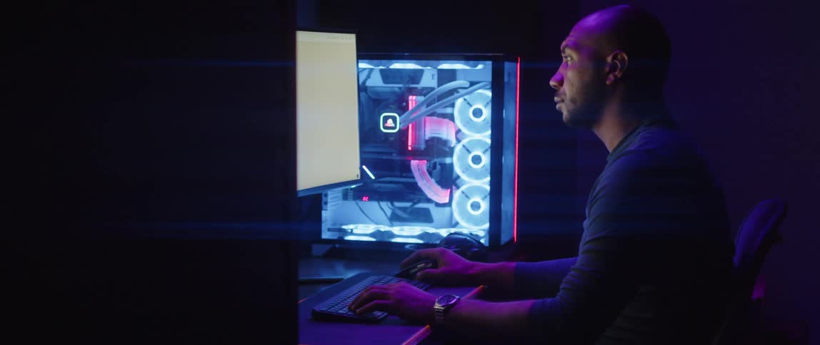 A man in an office sits in front of a computer and looks at equipment beside him and then back at his monitor