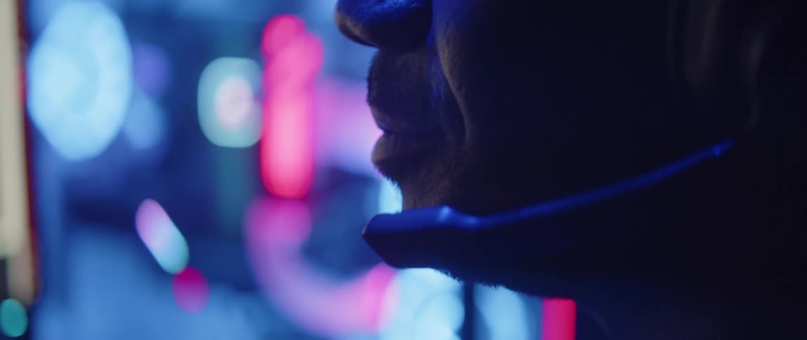 A man is speaking into a microphone on his headset as lights glow in the distance