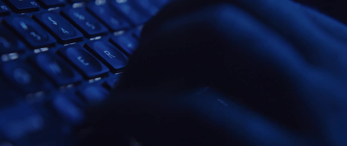 Mans fingers type on computer keyboard in dark room