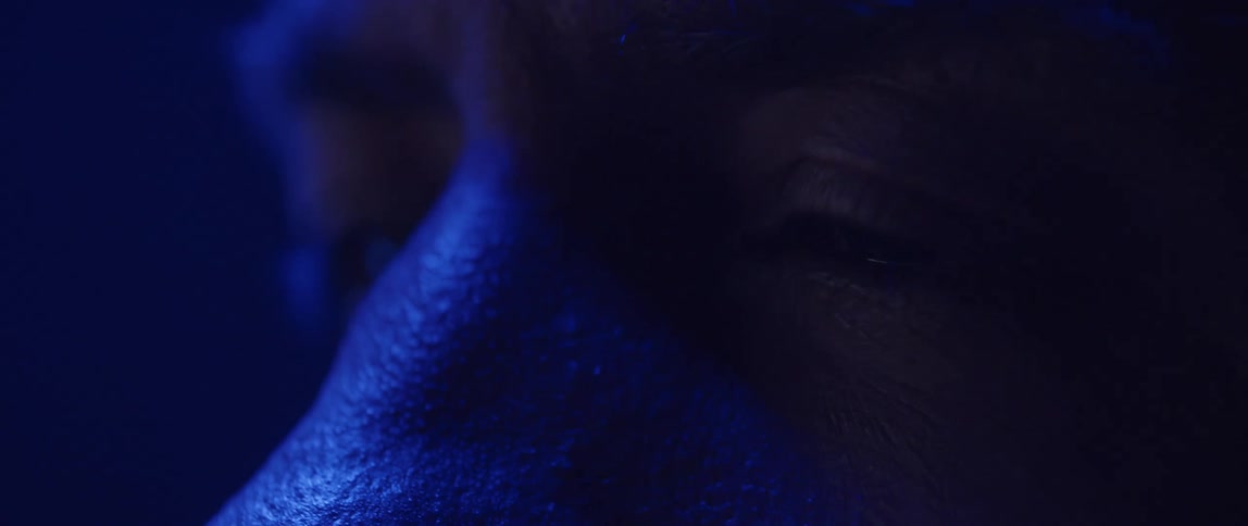 Mans face is tinted various colors as colored lighting changes shades