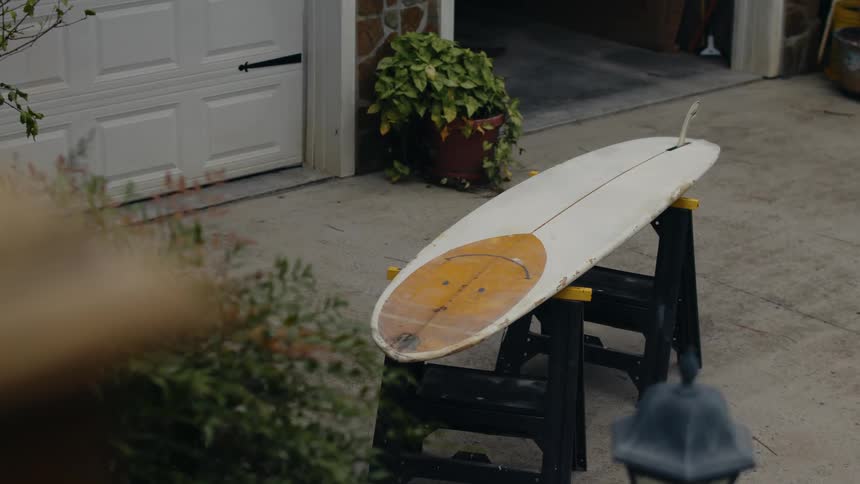 Surfboard sits on two a frame benches on driveway near an open two car garage