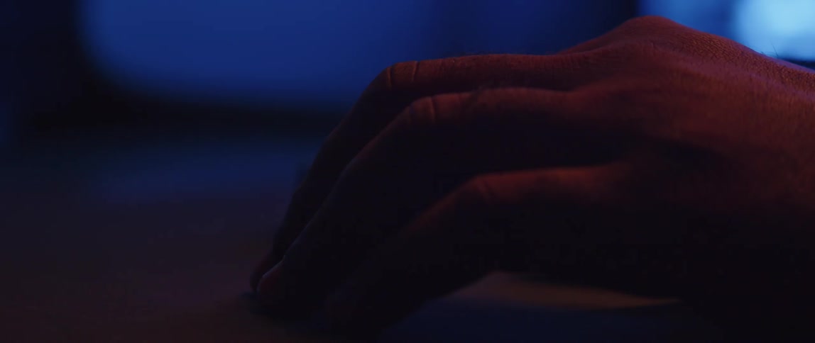 Colored lighting changes shades as person taps the desktop before moving hand back to computer keyboard