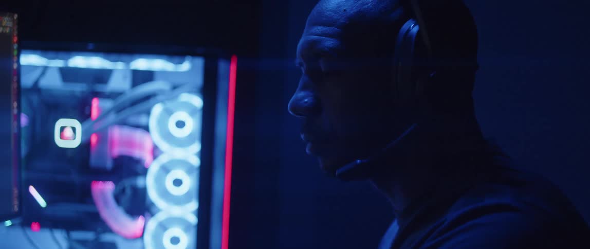 Man sitting in front of a computer under bright colorful rgb lights lowers the microphone on a headset