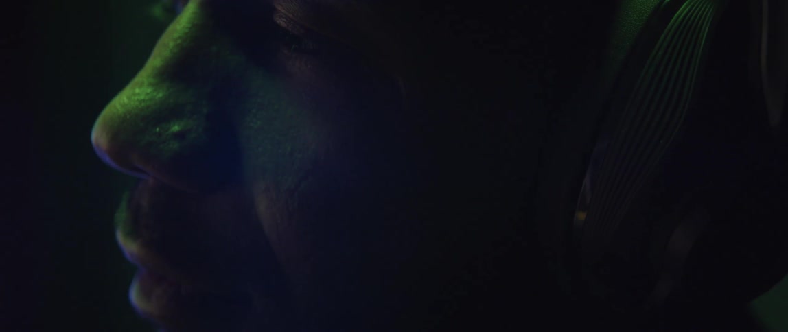Close up of the face of a man with his eyes closed wearing a headset under changing colorful lights