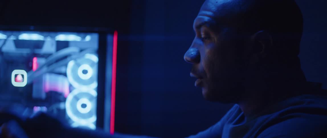 Man sitting in front of a computer under bright colorful rgb lights takes off a headset