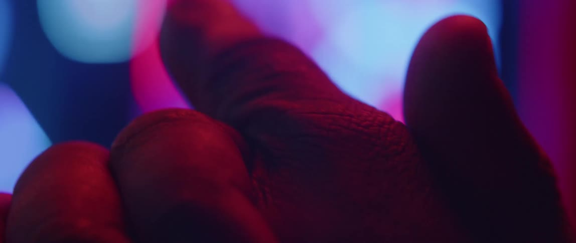 A man rubs his hands together and flexes his finger while colorful lights flash and glow