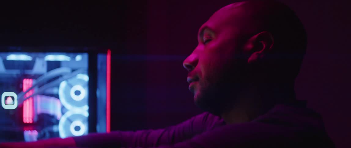 Man sitting in dim room near computer monitors stretches his arms and his neck