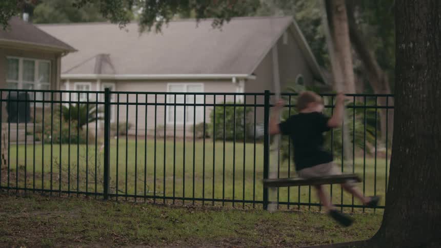 A child kicks against a tree to swing himself in a tree swing in the yard of a house during the day