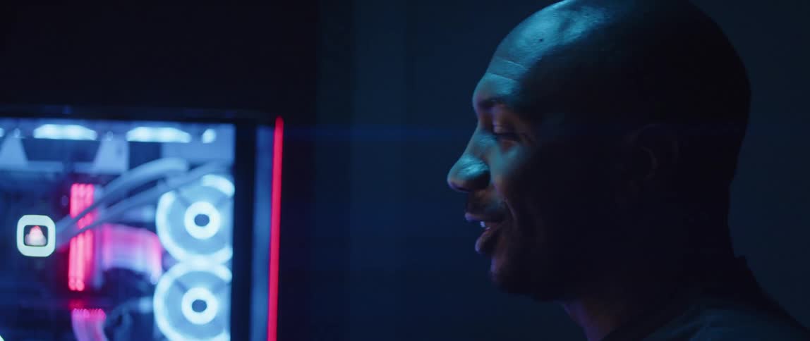 Man sits near display and smiles as he talks in dim room lit by colored lighting