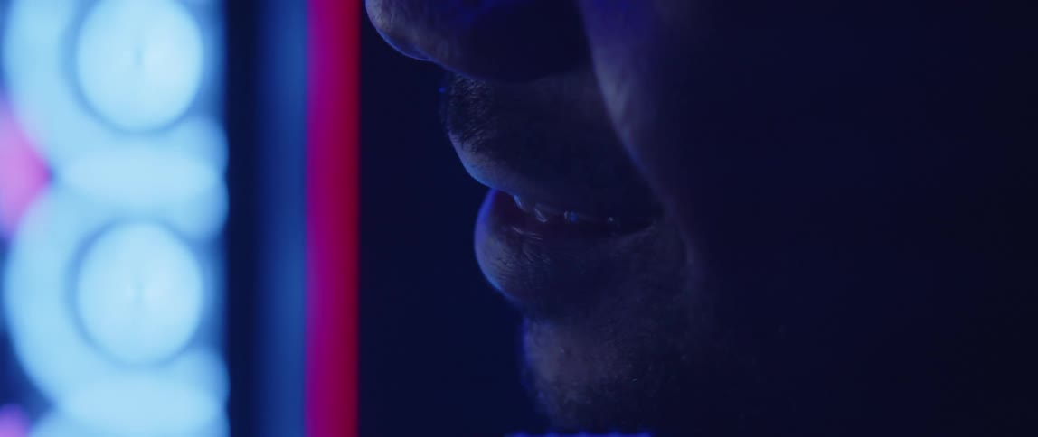 A man wearing a headset talks into microphone as lights flash and glow in the background