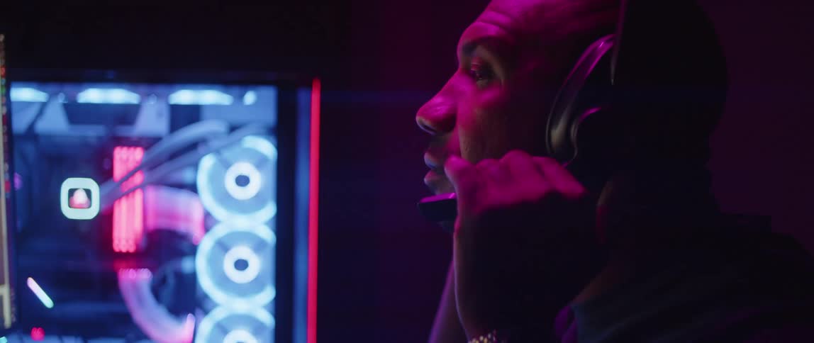 Bald man with silver wrist watch wears headphones next to pc case in dark room