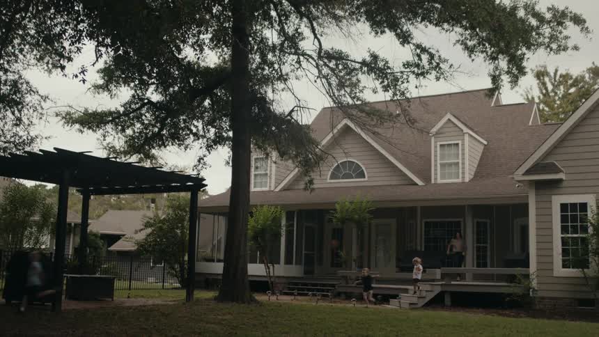 Three small children run out of a house and their mother is behind them and she sits on the porch