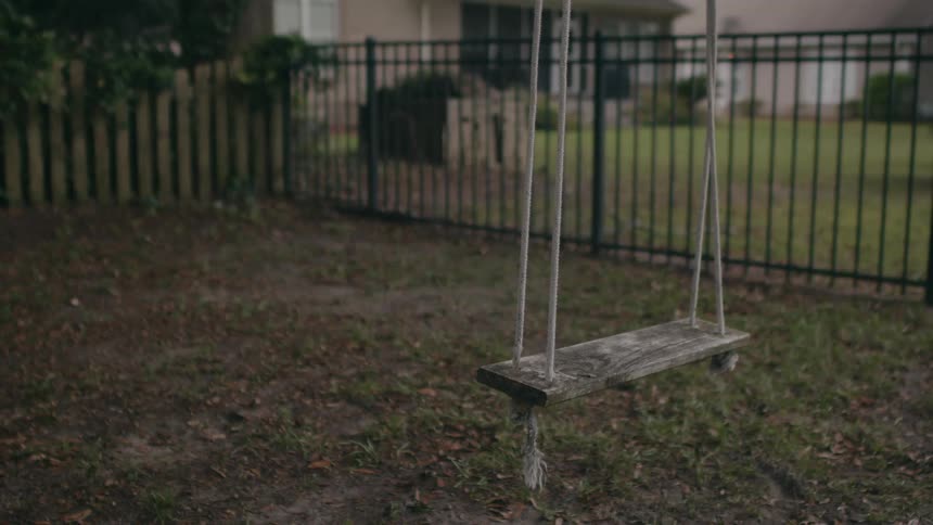 Wood swing with ropes next to iron fences in the garden