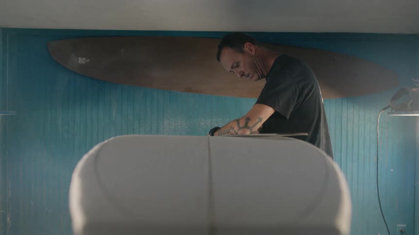 Man with tattoo black watch and t shirt makes a surfboard in surfboard shop