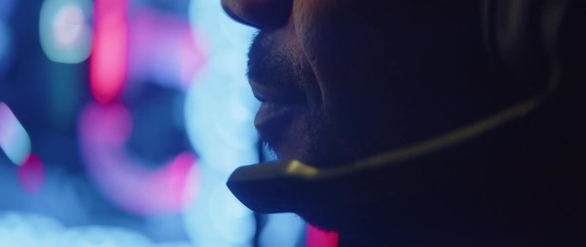 A man wearing a headset talking into the attached microphone while colorful lights glow