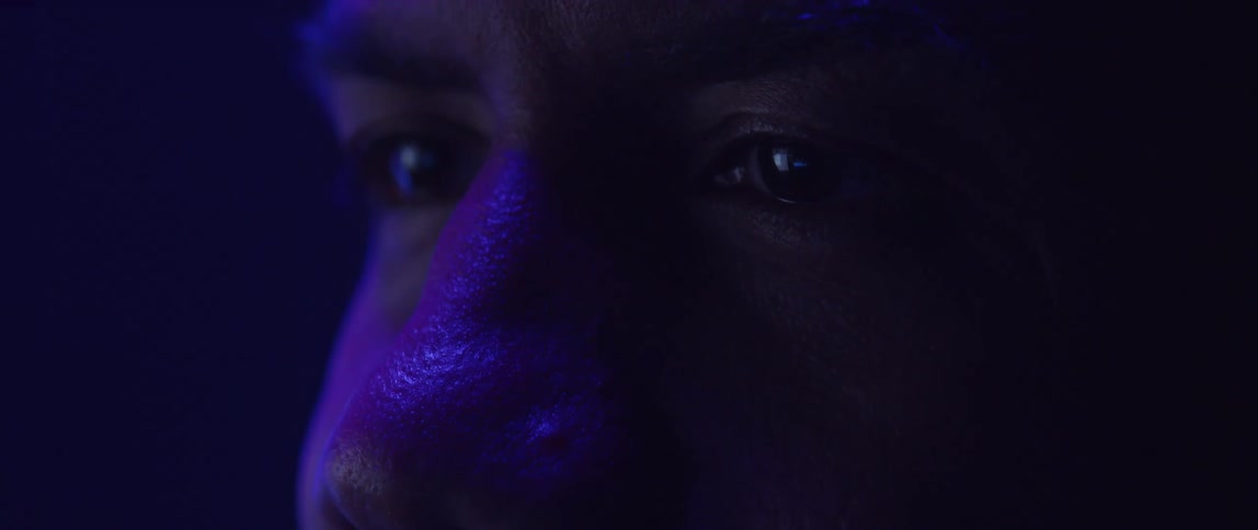 Close up of the eyes of a man looking at a screen under changing colorful rgb lights