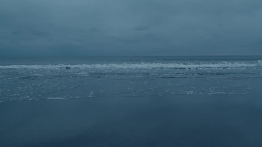 The tide washes into a sandy beach under a cloudy evening sky