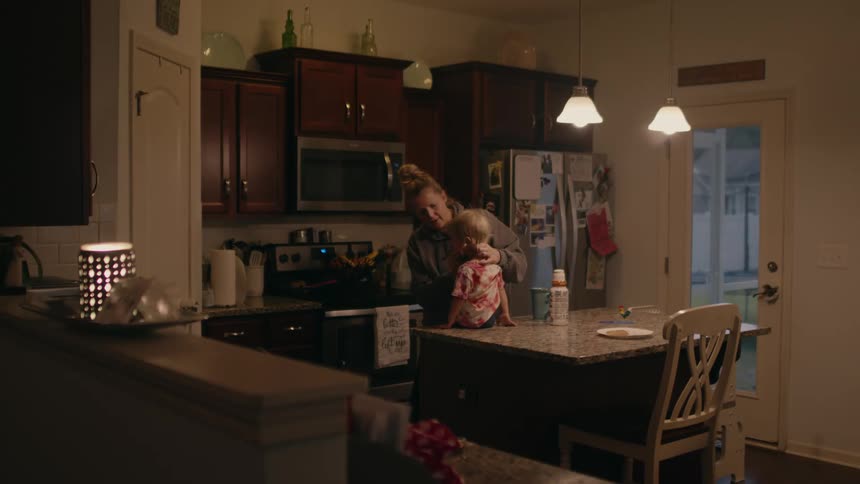 A woman picks up her daughter and places her on their kitchen island