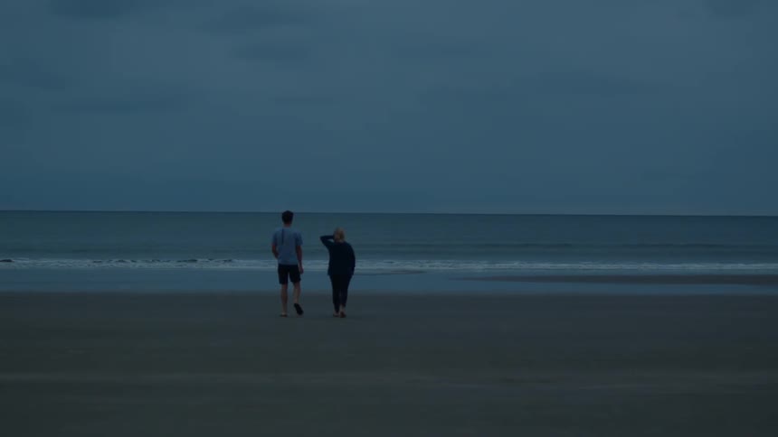 A man and woman chat while walking on the beach toward the ocean