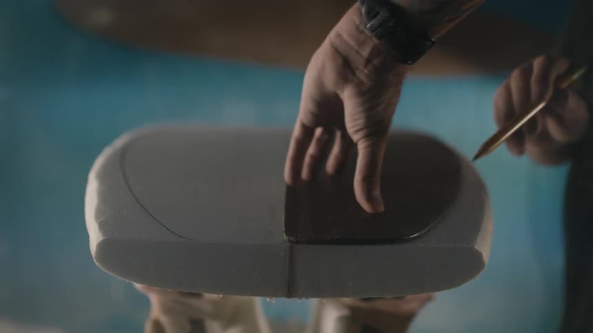 Man with black t shirt and watch creates a template on plywood by tracing a surfboard onto it