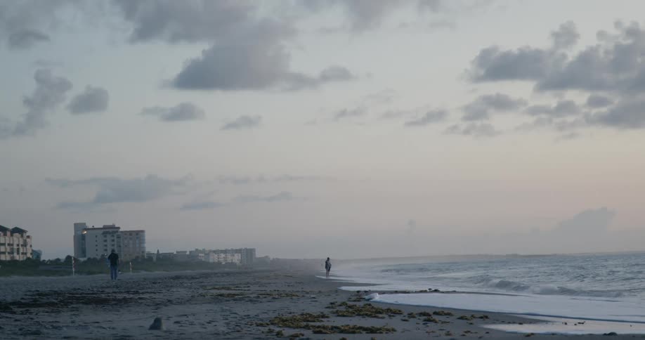 People stand on beach with the apartment buildings in the background as surf rolls onto beach