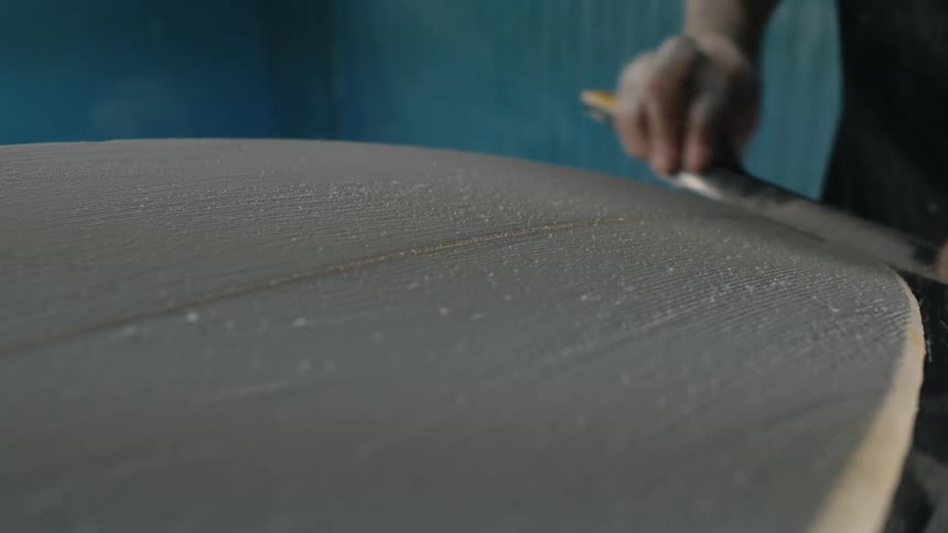 A man is holding a metal tool and using it to sand the piece of wood he is working on